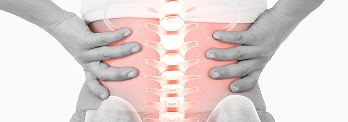 A person holding their lower back. Their spine is highlighted red.