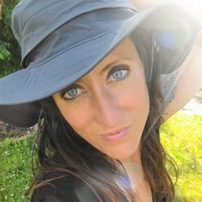 Kelly Troup smiling while wearing a hat outside.